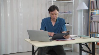 Modern dizüstü bilgisayar kullanan üst düzey Asyalı işadamı üretken ve odaklanmış bir kişi masasındaki mali grafik kağıdına özenle yazı yazıyor..