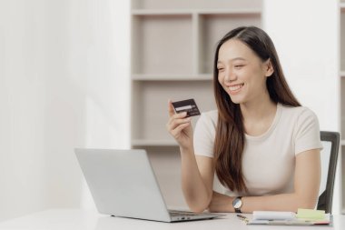 Çekici Asyalı kadın bilgisayarında akıllı telefon ve kredi kartı tutuyor. Cep telefonu bankacılığı ya da internet üzerinden alışveriş uygulaması kullanıyor.