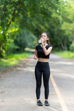 Spor kıyafetli genç ve güzel bir Asyalı kadın antrenman hazırlıklarına başlamadan önce kendini yenilemek için bir su şişesi açıyor. Su içen kadına odaklan.
