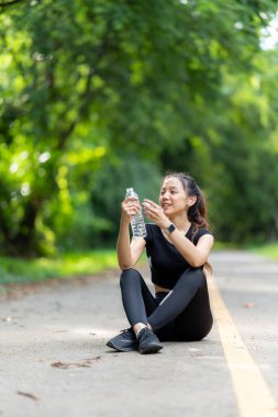 Spor kıyafetli genç ve güzel bir Asyalı kadın antrenman hazırlıklarına başlamadan önce kendini yenilemek için bir su şişesi açıyor. Su içen kadına odaklan.