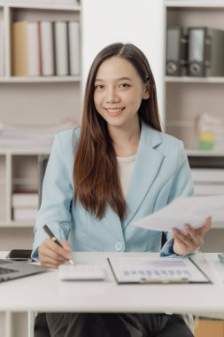 Asya 'lı iş kadını, finansal raporları analiz etmek için hesap makinesi dokümanlarıyla dizüstü bilgisayar pazarlama raporu kullanıyor.