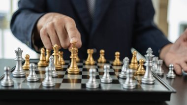 Takım elbiseli bir işadamının elleri başarılı bir maçta satranç taşlarını oynatıyor. İş stratejisi.