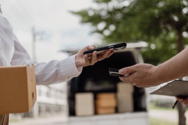 Genç bir adam, evinin önünde duran genç bir kadına karton bir kutu veriyor. Karton bir kutu tut ve sipariş verene ver ve akıllı telefonla öde..
