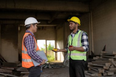 Foreman, mühendis ya da mimar, tamamlanmamış bir binanın inşaat alanındaki gayrimenkul inşaatının detaylarını kontrol etmek için elinde dizüstü bilgisayar ve planlar tutuyor.