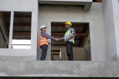 İnşaat alanında el ele tutuşan gülümseyen mühendisler ve el ele tutuşan mutlu mimarlar. Afrika inşaat yöneticisi takım çalışması. İşbirliği. Başarılı işbirliği kavramı.
