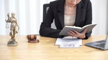 Ofiste ya da mahkemede çalışan Asyalı kadın avukat çekiç ve adalet ölçeği tabletiyle masada pirinç ölçekli sözleşme belgeleriyle birlikte ofis ve hukuk masasında çalışıyor.