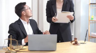 Asyalı erkek ve kadın avukatlar hukuki istişareleri tartışıyor, çekiç ve adalet terazisiyle çalışıyorlar..