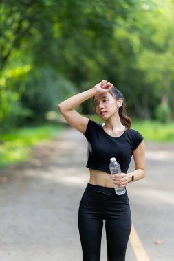 Spor kıyafetiyle egzersiz yapmadan ve içme suyu içmeden önce hazırlanan genç bir kadın modelin resmi. Çalışmaya başlamadan önce ferahlamak için bir şişe temiz su açın..