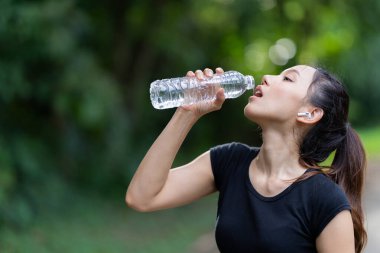 Spor kıyafetiyle egzersiz yapmadan ve içme suyu içmeden önce hazırlanan genç bir kadın modelin resmi. Çalışmaya başlamadan önce ferahlamak için bir şişe temiz su açın..