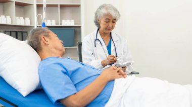 Üst düzey Asyalı erkek hasta yıllık muayenesi için doktoru ziyaret ediyor. Yaşlılara bakmakla görevli bakıcılar, yataktaki hastanelere, ilaçlara, sağlık hizmetlerine ve hayat sigortasına yardım ederler.