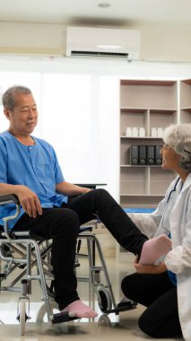 Yaşlı Asyalı bir adam, kıdemli bir kadın terapist hemşirenin desteğiyle fizik tedavi görüyor. Yaşlı adam evde bakım ve sağlık hizmetleri konseptinde hasta için elastik bant kullanıyor..