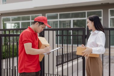 Kırmızı elbiseli genç kurye karton bir paket kutusu tutuyor ve kadınlar paketleri evden, online alışveriş ve mal teslimatından almak için cep telefonuyla para transfer ediyorlar..