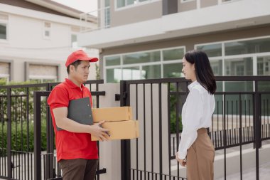 Kırmızı elbiseli genç kurye karton bir paket kutusu tutuyor ve kadınlar paketleri evden, online alışveriş ve mal teslimatından almak için cep telefonuyla para transfer ediyorlar..