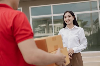 Kırmızı elbiseli genç kurye karton bir paket kutusu tutuyor ve kadınlar paketleri evden, online alışveriş ve mal teslimatından almak için cep telefonuyla para transfer ediyorlar..