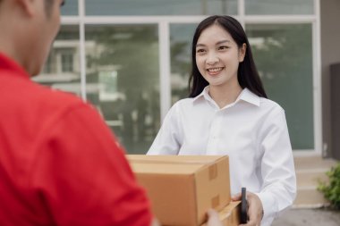 Kırmızı elbiseli genç kurye karton bir paket kutusu tutuyor ve kadınlar paketleri evden, online alışveriş ve mal teslimatından almak için cep telefonuyla para transfer ediyorlar..