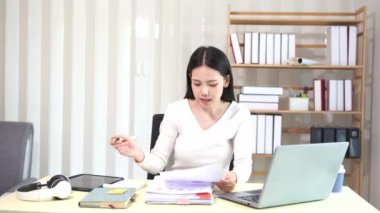 Evinde dizüstü bilgisayarlı finansal belgelerle çalışan Asyalı iş kadını pazarlamayı analiz ediyor, aylık muhasebe ve çizelgeler yapıyor. Ofiste. Evde çalış..