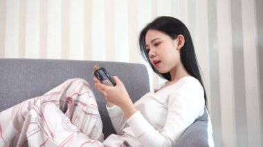 Genç Asyalı bir kadın, plastik bir kredi kartıyla ev telefonunun rahatlığıyla online alışveriş yapıyor. Evde para transferi, oturma odasında kanepede oturan güzel bir kadın.