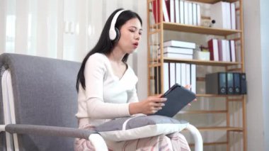 Asyalı kız tabletle mutlu bir şekilde oynuyor, rahat bir koltukta oturuyor, online alışveriş yapıyor sosyal medya uygulamalarını kullanarak internette sörf yapıyor ya da modern teknoloji cihazlarıyla oyunlar oynuyor..