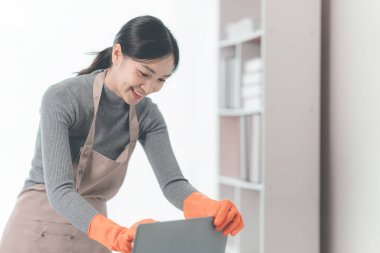 Asya Bayan önlük ev ev işleri yaparak. Elektrikli süpürge oturma odasında ahşap zemin temizlik kullanarak genç ev hanımı. mutlu ev kadını evde yüz çekici gülümseme ile temizlemenizi.