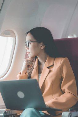 Uçuş, seyahat ve turizm konularında pencere kenarında çalışan Asyalı iş kadını, laptopla uçuş sırasında uçak kabininde çalışan başarılı Asyalı kadın.