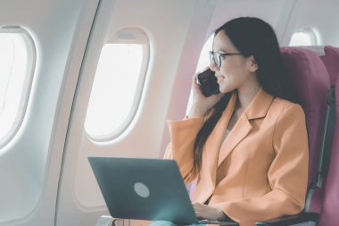 Uçuş, seyahat ve turizm konularında pencere kenarında çalışan Asyalı iş kadını, laptopla uçuş sırasında uçak kabininde çalışan başarılı Asyalı kadın.