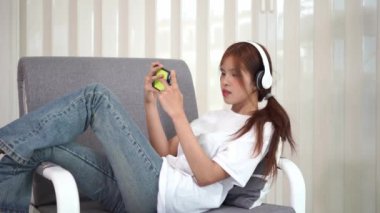 Mutlu genç Asyalı kadın evdeki yumuşak bir kanepede dinleniyor. Akıllı telefonda sohbet mesajları yazmak, cep telefonuyla sohbet etmek, sosyal medyada oynamak. İnternet 'te bilgi ara