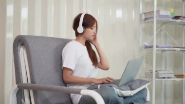 Uzaktan çalışan Asyalı bir kadın uzaktan kumandalı bir etkinliğin tadını çıkararak masaya oturmuş gülümsüyor. Sosyal ağlarda sohbet etmek, dizüstü bilgisayar ve finansal belgeler kullanmak, evde çalışmak..