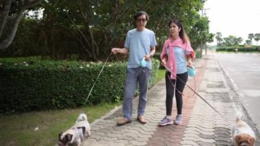 Yaşlı bir çift, küçük köpekleriyle parkta bir patikada yürüyor, köpekle birlikte doğada dinleniyorlar. Yaşlı erkek ve kadının tüm vücudu şık ve modaya uygun.