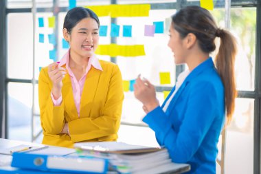 İki Asyalı iş kadını, iş arkadaşlarıyla verimli bir diyalog için bilgisayarlarını ve tabletlerini kullanarak evrak, mali grafikler analiz ediyor, ofiste çalışıyor..