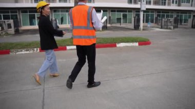 Asyalı emlak işadamı konut projesini teftiş ediyor. Genç bir çift ev inşaatının planını tartışıyor ve inceliyor..