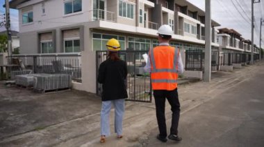 Asyalı emlak işadamı konut projesini teftiş ediyor. Genç bir çift ev inşaatının planını tartışıyor ve inceliyor..