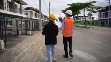 Asyalı emlak işadamı konut projesini teftiş ediyor. Genç bir çift ev inşaatının planını tartışıyor ve inceliyor..