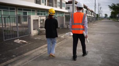 Asyalı emlak işadamı konut projesini teftiş ediyor. Genç bir çift ev inşaatının planını tartışıyor ve inceliyor..