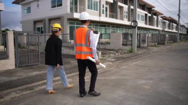 Asyalı emlak işadamı konut projesini teftiş ediyor. Genç bir çift ev inşaatının planını tartışıyor ve inceliyor..