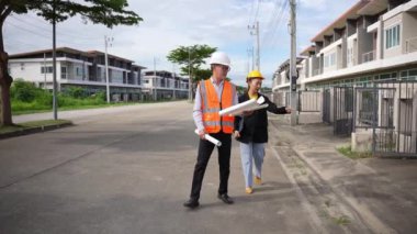 Asyalı emlak işadamı konut projesini teftiş ediyor. Genç bir çift ev inşaatının planını tartışıyor ve inceliyor..