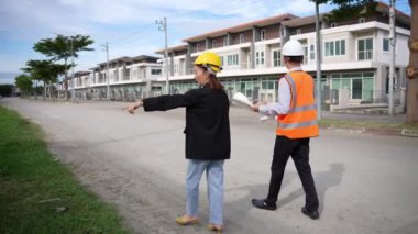 Asyalı emlak işadamı konut projesini teftiş ediyor. Genç bir çift ev inşaatının planını tartışıyor ve inceliyor..