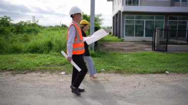Asyalı emlak işadamı konut projesini teftiş ediyor. Genç bir çift ev inşaatının planını tartışıyor ve inceliyor..