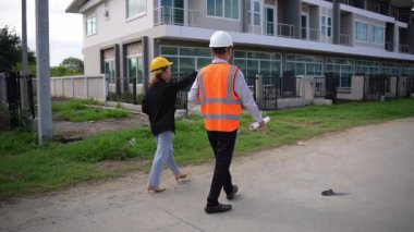 Asyalı emlak işadamı konut projesini teftiş ediyor. Genç bir çift ev inşaatının planını tartışıyor ve inceliyor..