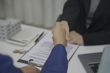 Emlakçı, iş genişletme ve köy inşaat projesine yatırım için bütçe anlaşmasından sonra müşteriyle tokalaşıyor, emlak finans kavramını kapatıyor..