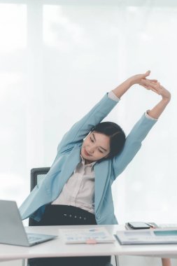 Güzel Asyalı iş kadını çalışırken ellerini uzatıyor ve iş yorgunluğundan dinleniyor. Muhasebe raporları üzerinde çalışırken ellerini uzatıyor.