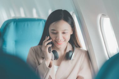 Uçak camındaki Asyalı kadın akıllı telefonla konuşurken cep telefonu kullanıyor. Bir insan işi hakkında konuşuyor..