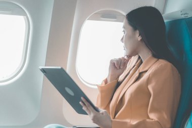 Genç Asyalı kadın çalışmak ya da işe hazırlanmak için dizüstü bilgisayar kullanıyor uçakta seyahat ederken, bilgisayardan alışveriş yaparken, uçuş sırasında pencerenin yanında otururken..