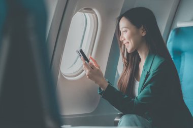 Uçak camındaki Asyalı kadın akıllı telefonla konuşurken cep telefonu kullanıyor. Bir insan işi hakkında konuşuyor..