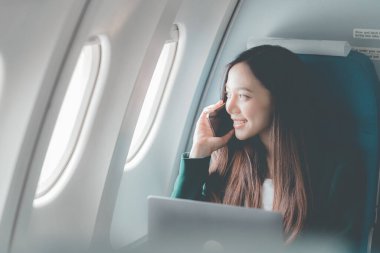 Uçak camındaki Asyalı kadın akıllı telefonla konuşurken cep telefonu kullanıyor. Bir insan işi hakkında konuşuyor..