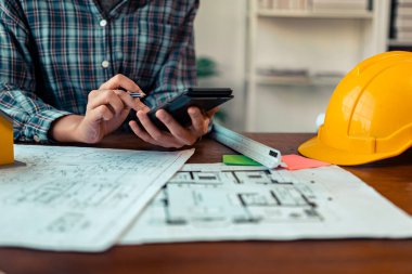 Mimarlar ve mühendisler, inşaat planlarını tartışmak üzere bina içindeki mimari çizimlerin ayrıntılı planlarına ve etrafa saçılmış mimar şapkaları ve mimari belgelere işaret ediyorlar. Yakın plan..