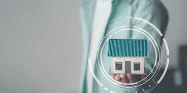 Elle korunan tahta oyuncak ev, ev sigortası konsepti, emlakçı ve müşteriyle ev modeli ev satın alma sözleşmesi, sigorta veya emlak kredisi tartışması.