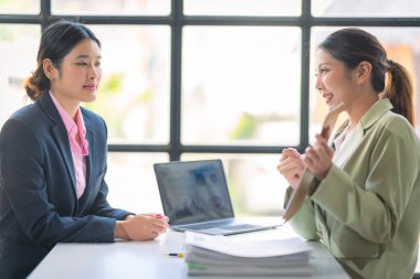 Ticari veri analizinde finansal veri grafik belgeleri ve dizüstü bilgisayarlarla çalışan iki başarılı Asyalı iş kadını.