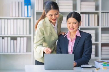 Ticari veri analizinde finansal veri grafik belgeleri ve dizüstü bilgisayarlarla çalışan iki başarılı Asyalı iş kadını.