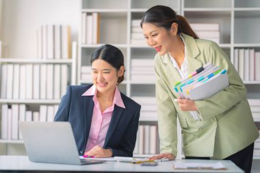 Ticari veri analizinde finansal veri grafik belgeleri ve dizüstü bilgisayarlarla çalışan iki başarılı Asyalı iş kadını.