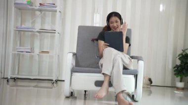 Genç Asyalı kadın elinde dijital tabletle kanepede oturmuş internette sörf yapıyor, sosyal medya uygulaması kullanarak online alışveriş yapıyor..